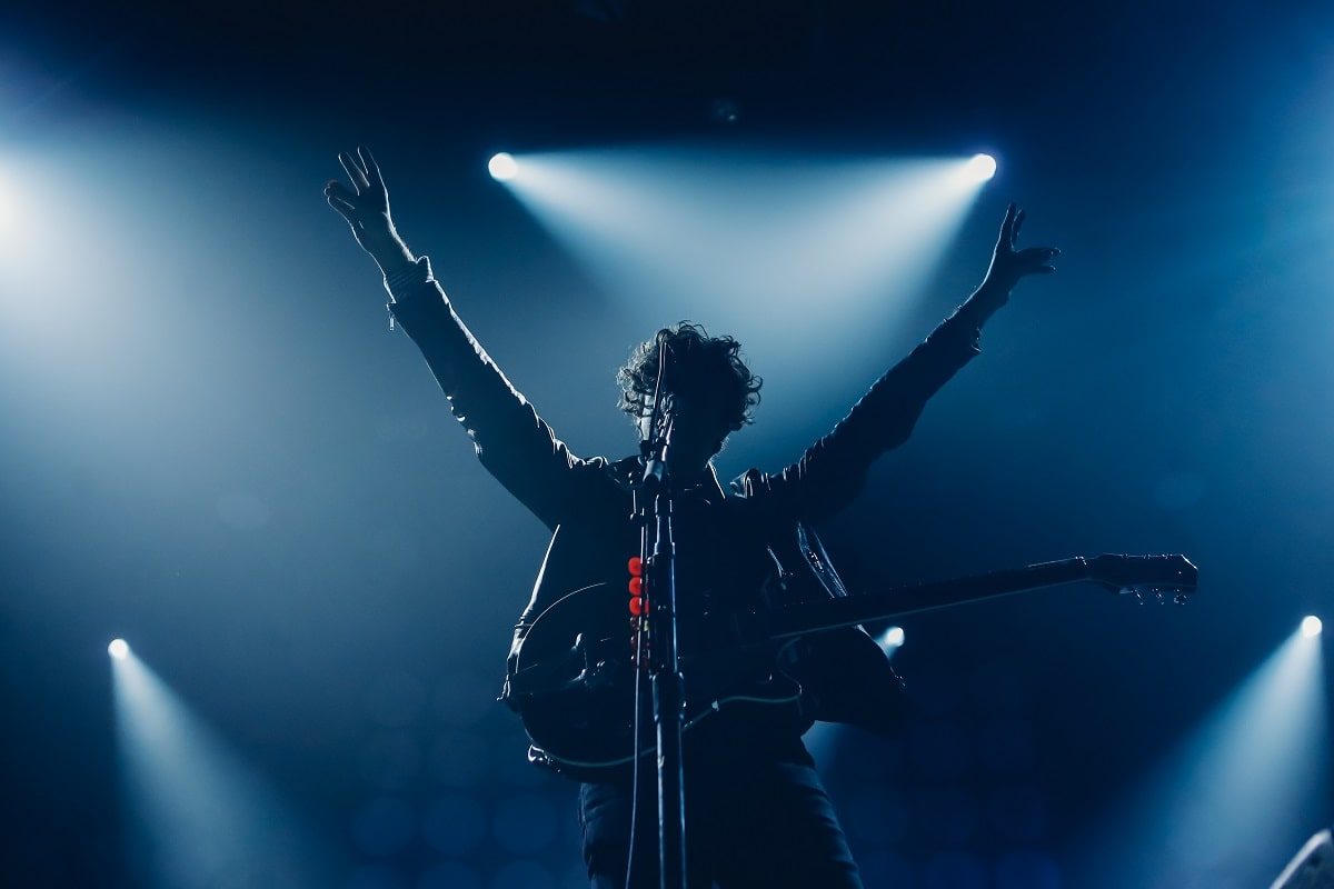Guitarist with arms raised in blue stage light